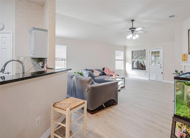 living room with baseboards, ceiling fan, light wood finished floors, and visible vents