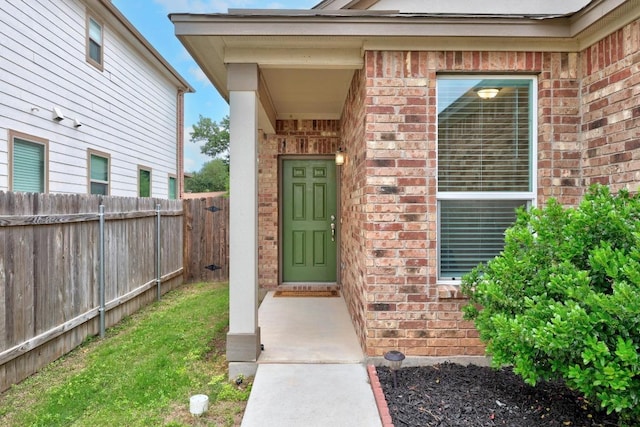view of exterior entry with fence and brick siding