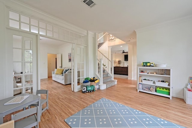 interior space with visible vents, ornamental molding, stairs, wood finished floors, and ceiling fan with notable chandelier