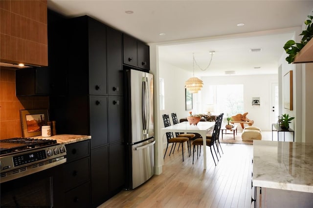kitchen with light wood-style floors, appliances with stainless steel finishes, dark cabinetry, and light stone counters