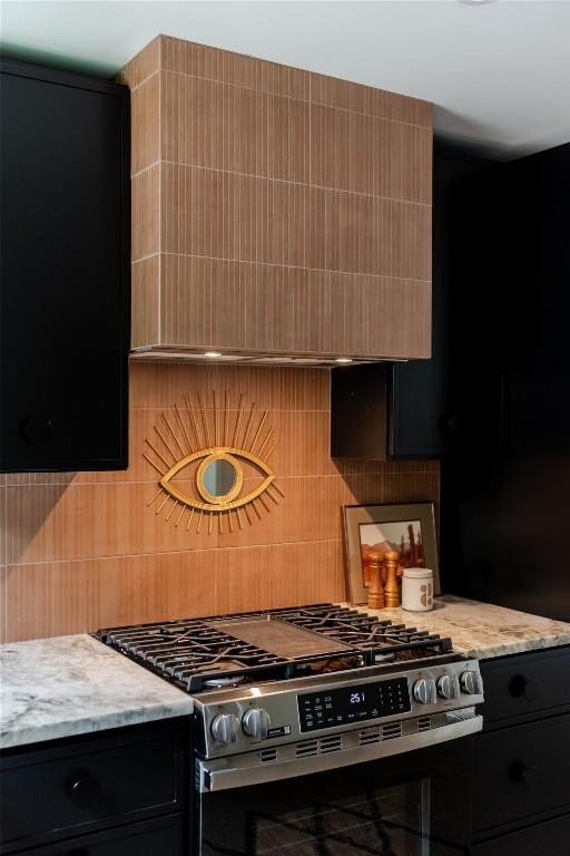 kitchen with light stone counters, backsplash, and stainless steel gas range oven