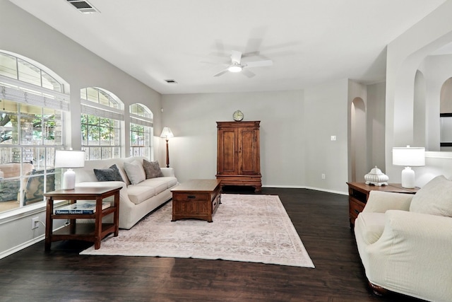 living room with a ceiling fan, arched walkways, visible vents, and dark wood finished floors