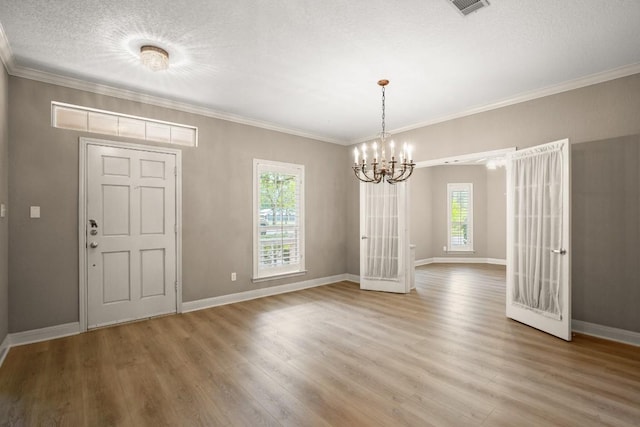 unfurnished dining area with crown molding, an inviting chandelier, light wood-style flooring, baseboards, and visible vents