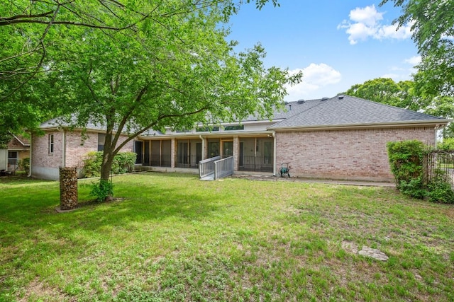 back of house featuring a sunroom, a lawn, roof with shingles, and brick siding