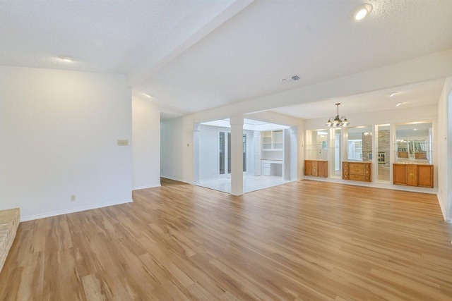 unfurnished living room featuring an inviting chandelier, visible vents, baseboards, a textured ceiling, and light wood finished floors