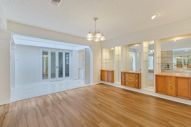 interior space with light wood-style floors, a textured ceiling, a notable chandelier, and visible vents