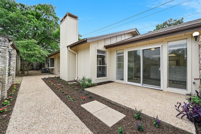 rear view of property with fence, a patio, a chimney, central AC unit, and board and batten siding