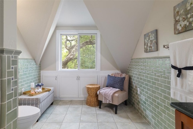 interior space with a wainscoted wall, vaulted ceiling, tile patterned floors, and tile walls