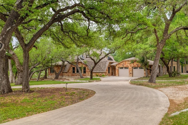 view of front of house with curved driveway, an attached garage, and stone siding