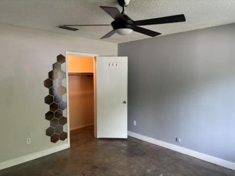 unfurnished bedroom with baseboards, a textured ceiling, a walk in closet, and concrete floors