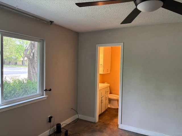 interior space featuring baseboards, connected bathroom, a textured ceiling, and ceiling fan