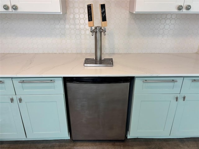 room details featuring stainless steel dishwasher, light stone counters, decorative backsplash, and blue cabinets