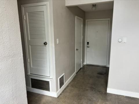 corridor featuring baseboards, concrete floors, and visible vents