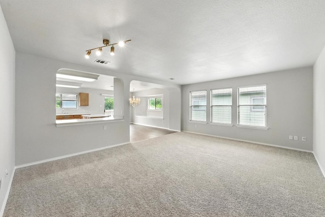 carpeted spare room with baseboards, a wealth of natural light, arched walkways, and a chandelier