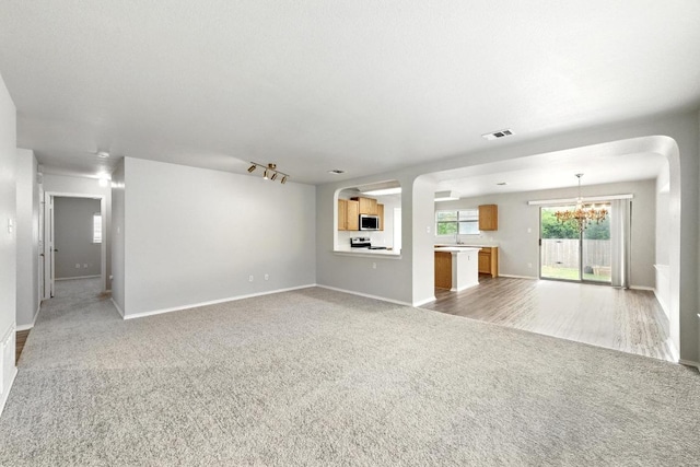 unfurnished living room with light colored carpet, arched walkways, baseboards, and an inviting chandelier