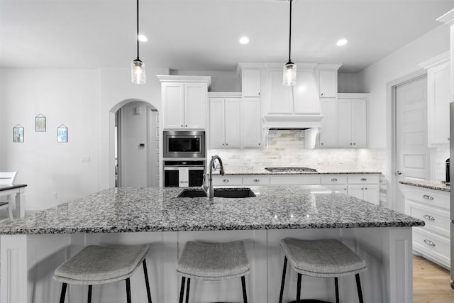 275 Axis Cir, Fredericksburg, TX 78624 - kitchen featuring appliances with stainless steel finishes, a sink, arched walkways, decorative backsplash, and white cabinetry