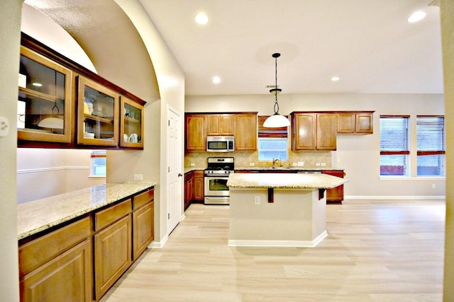 kitchen with light stone countertops, light wood-style floors, stainless steel appliances, decorative backsplash, and pendant lighting