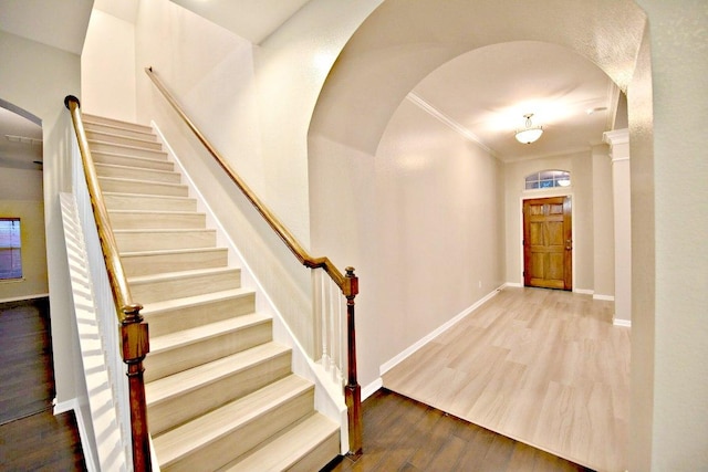 staircase featuring arched walkways, baseboards, ornamental molding, and wood finished floors