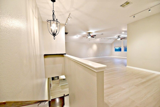 hallway with an upstairs landing, rail lighting, wood finished floors, and visible vents