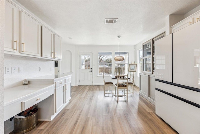 3405 Barksdale Dr, Austin, TX 78725 - kitchen with freestanding refrigerator, light wood-type flooring, white cabinets, light countertops, and a textured ceiling