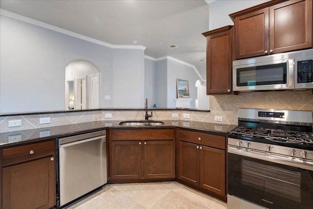 kitchen with crown molding, a sink, arched walkways, dark stone counters, and stainless steel appliances