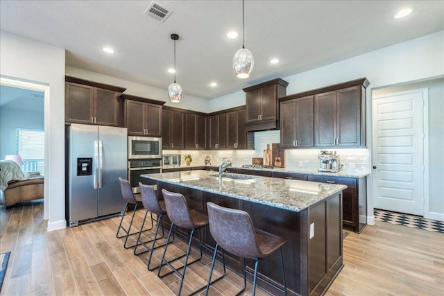 170 Alice Jane Ln, Buda, TX 78610 - kitchen with stainless steel appliances, light wood-style floors, dark brown cabinetry, light stone countertops, and recessed lighting