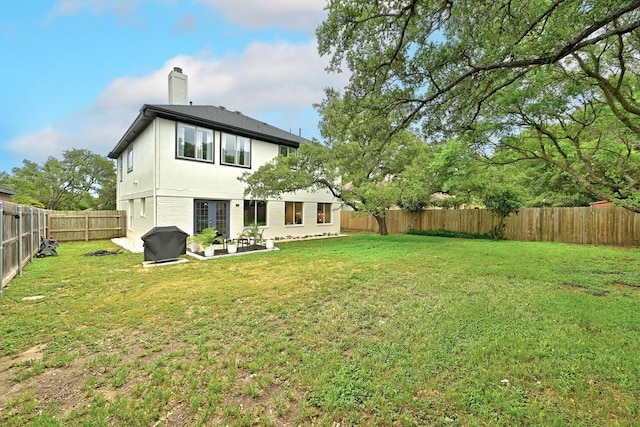 rear view of house with a chimney, a lawn, a patio area, a fenced backyard, and stucco siding
