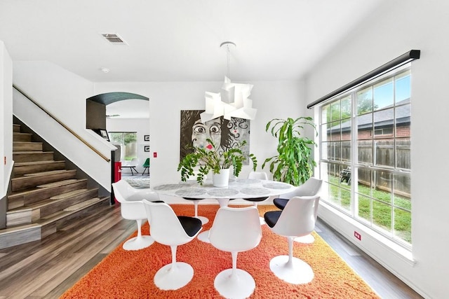 dining area featuring arched walkways, plenty of natural light, and wood finished floors
