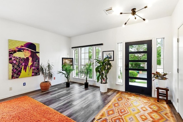 entryway with baseboards, a notable chandelier, visible vents, and wood finished floors