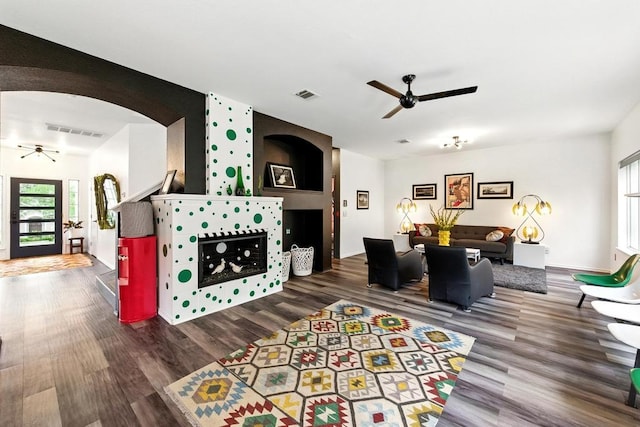 living area featuring arched walkways, ceiling fan, and visible vents