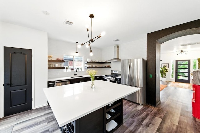 kitchen featuring open shelves, a sink, light countertops, wall chimney exhaust hood, and stainless steel appliances