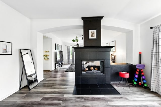 living area featuring arched walkways, a fireplace, vaulted ceiling, and wood finished floors