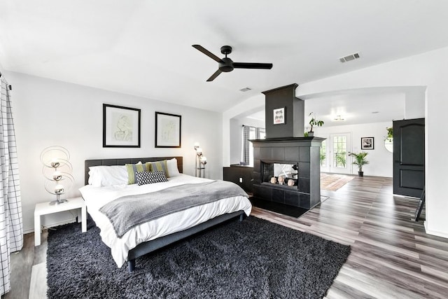 bedroom with a ceiling fan, visible vents, a fireplace, vaulted ceiling, and wood finished floors