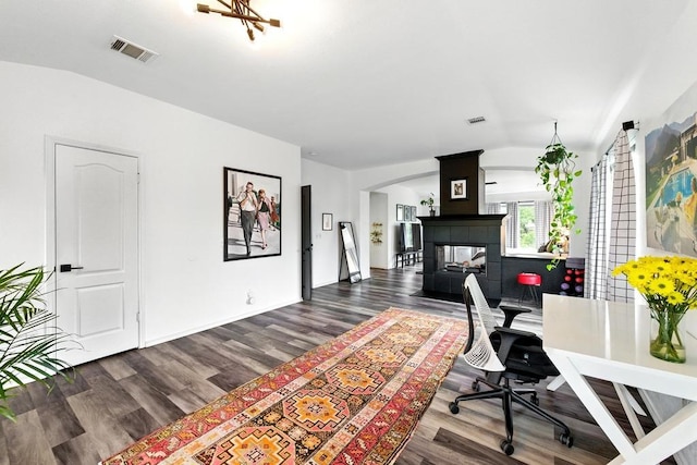 office area featuring visible vents, wood finished floors, a fireplace, arched walkways, and vaulted ceiling