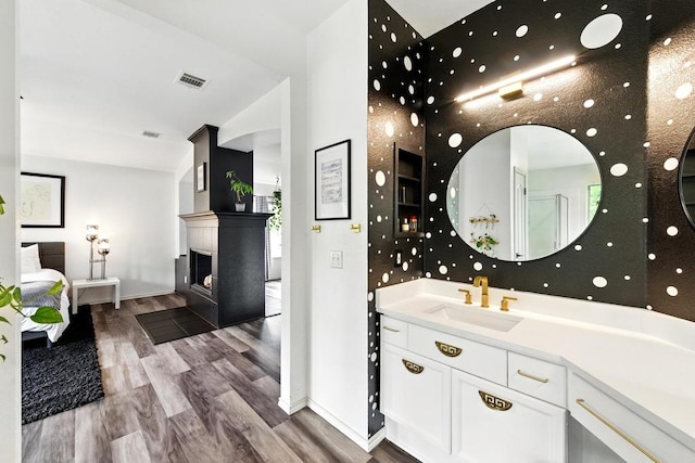 bathroom featuring visible vents, a fireplace, wood finished floors, baseboards, and vanity