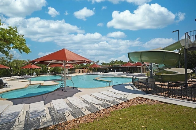 community pool featuring a patio, a water slide, and fence