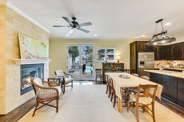 dining space featuring crown molding, ceiling fan, a tiled fireplace, recessed lighting, and wood finished floors