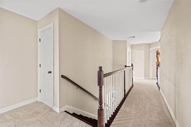 corridor featuring carpet floors, visible vents, baseboards, and an upstairs landing