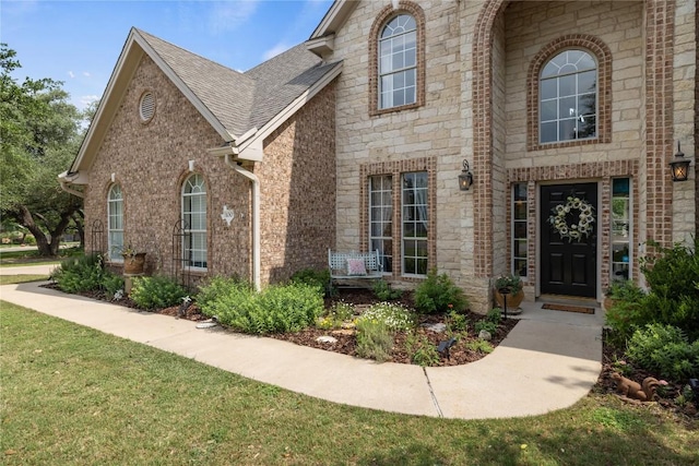 view of front of house with brick siding, stone siding, a front yard, and roof with shingles