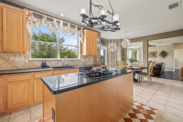 kitchen featuring an inviting chandelier, a sink, backsplash, gas stovetop, and a kitchen island