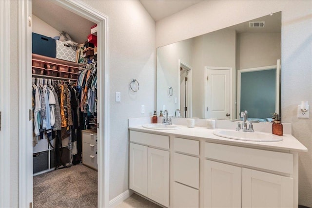full bathroom with double vanity, a walk in closet, visible vents, and a sink