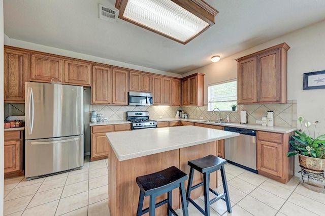 kitchen with appliances with stainless steel finishes, a sink, a kitchen breakfast bar, tasteful backsplash, and visible vents