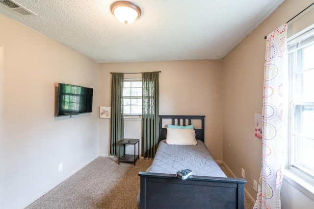 carpeted bedroom featuring baseboards, multiple windows, a textured ceiling, and visible vents