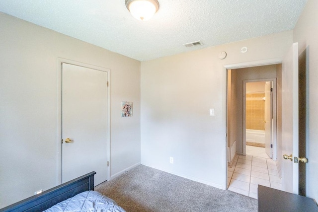 carpeted bedroom with a textured ceiling, visible vents, baseboards, and tile patterned flooring