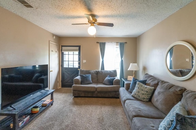 living room featuring carpet flooring, a textured ceiling, ceiling fan, and visible vents
