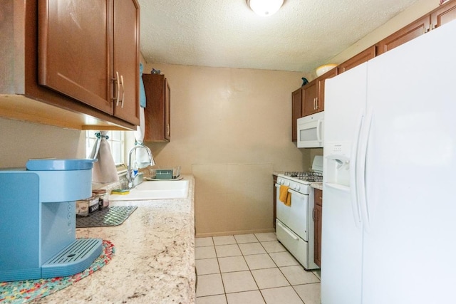 kitchen featuring white appliances, light countertops, a textured ceiling, a sink, and light tile patterned floors