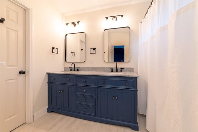 bathroom with double vanity, baseboards, a sink, and wood finished floors