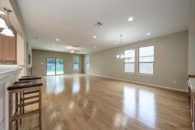 unfurnished living room featuring light wood-style floors, baseboards, ceiling fan with notable chandelier, and recessed lighting