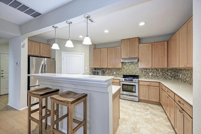 kitchen featuring a breakfast bar, light countertops, stainless steel appliances, under cabinet range hood, and visible vents