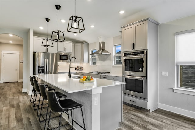 kitchen with wood finished floors, wall chimney exhaust hood, arched walkways, a sink, and appliances with stainless steel finishes